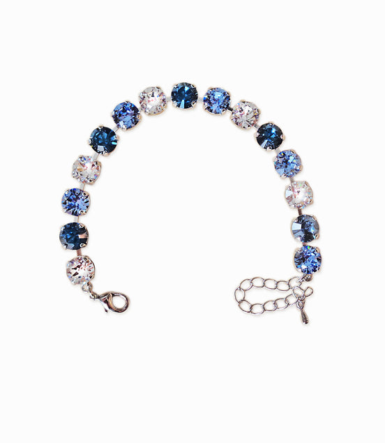 Bracelet with blue and clear gemstones on a white background.Made with genuine Austrian crystal it is a single row of crystals in colours clear crystal,light blueand dark blue.The bracelet is size medium and fits average wrist.It includes an extension chain.The metal is rhodium silver plated nickel free